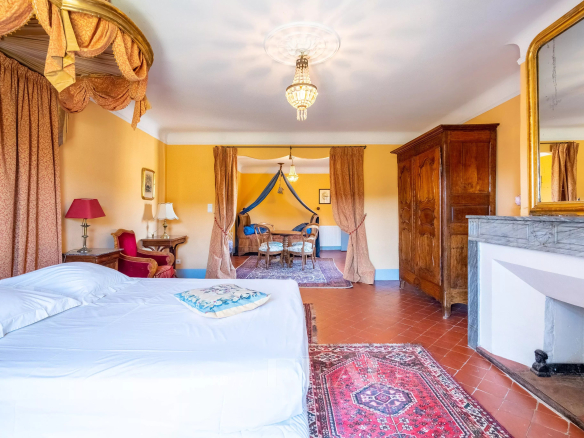 Intérieur d'une chambre spacieuse avec lit, fauteuils et cheminée dans un château du XVIIème siècle à Valensole.