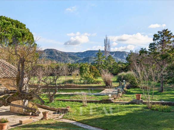 View of a Provençal farmhouse with wooded grounds and mountains in the background in Cavaillon.