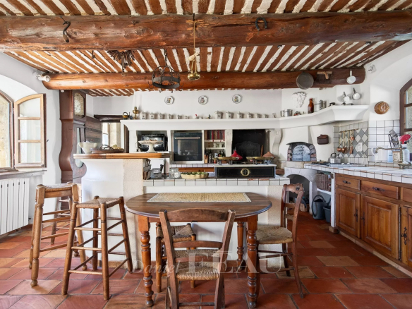 Interior of a Provençal farmhouse with rustic kitchen, wooden table and exposed beams.
