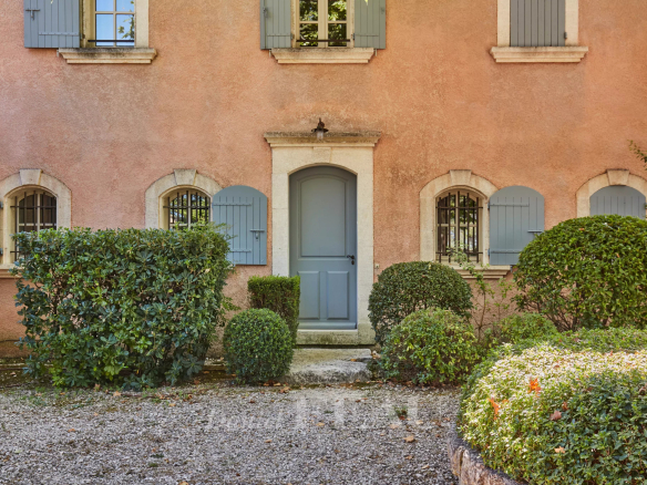 Façade d'une maison d'architecte en pierre rose avec porte bleue et jardin paysager à Saint-Rémy-de-Provence.