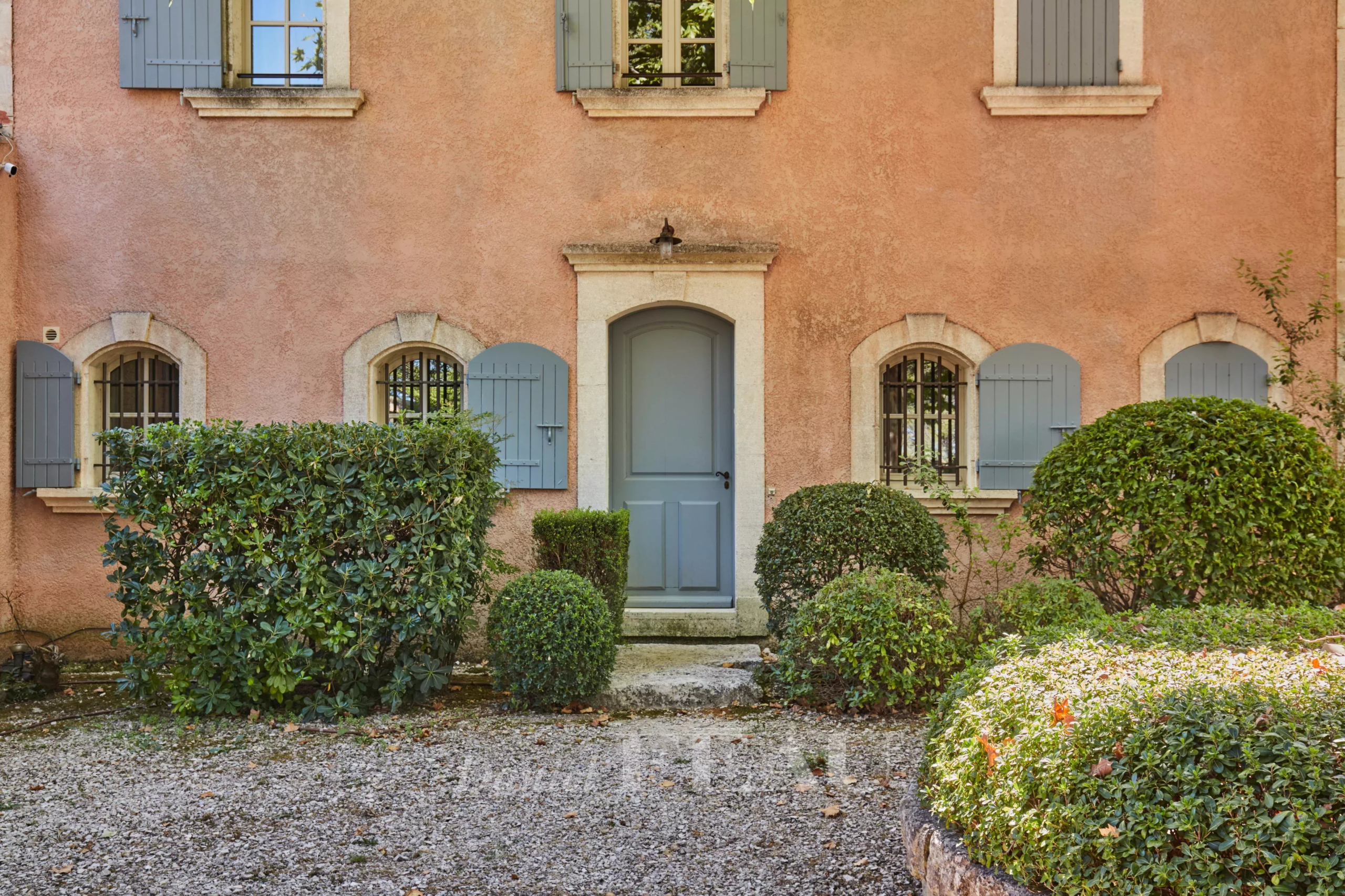 Façade d'une maison d'architecte en pierre rose avec porte bleue et jardin paysager à Saint-Rémy-de-Provence.