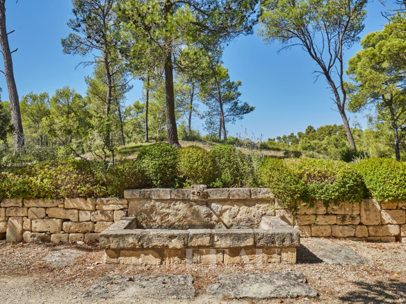 Fontaine en pierre dans un jardin paysager entouré d'arbres, à Saint-Rémy-de-Provence.