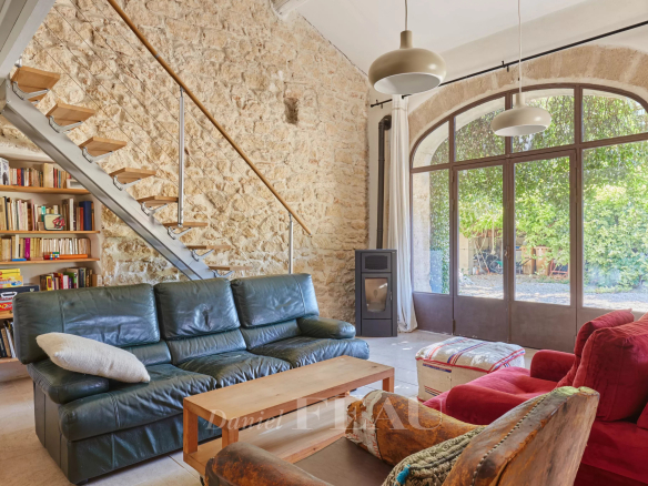 Intérieur d'un mas provençal avec poutres apparentes et murs en pierre, salon lumineux et escalier en bois.