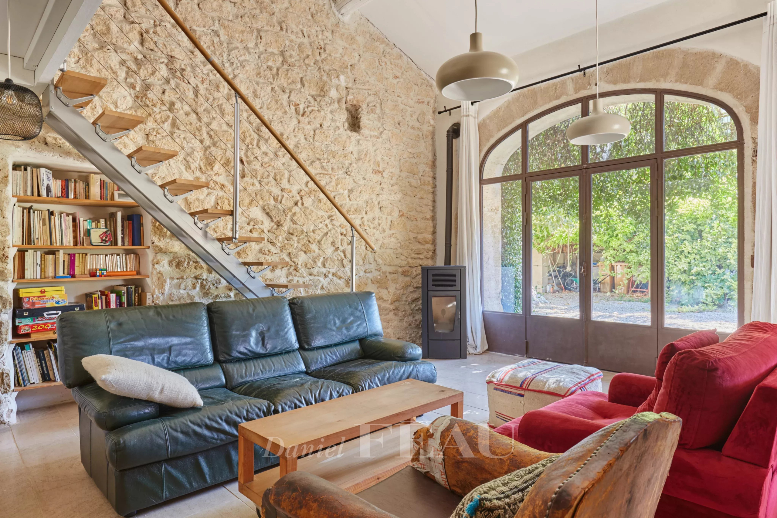 Intérieur d'un mas provençal avec poutres apparentes et murs en pierre, salon lumineux et escalier en bois.