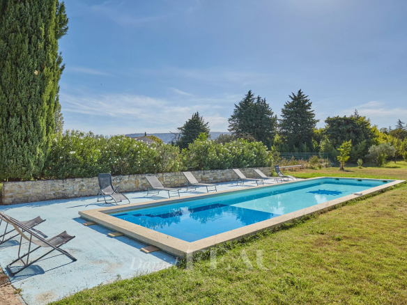 Piscine entourée de chaises longues dans un jardin verdoyant près d'un mas provençal.