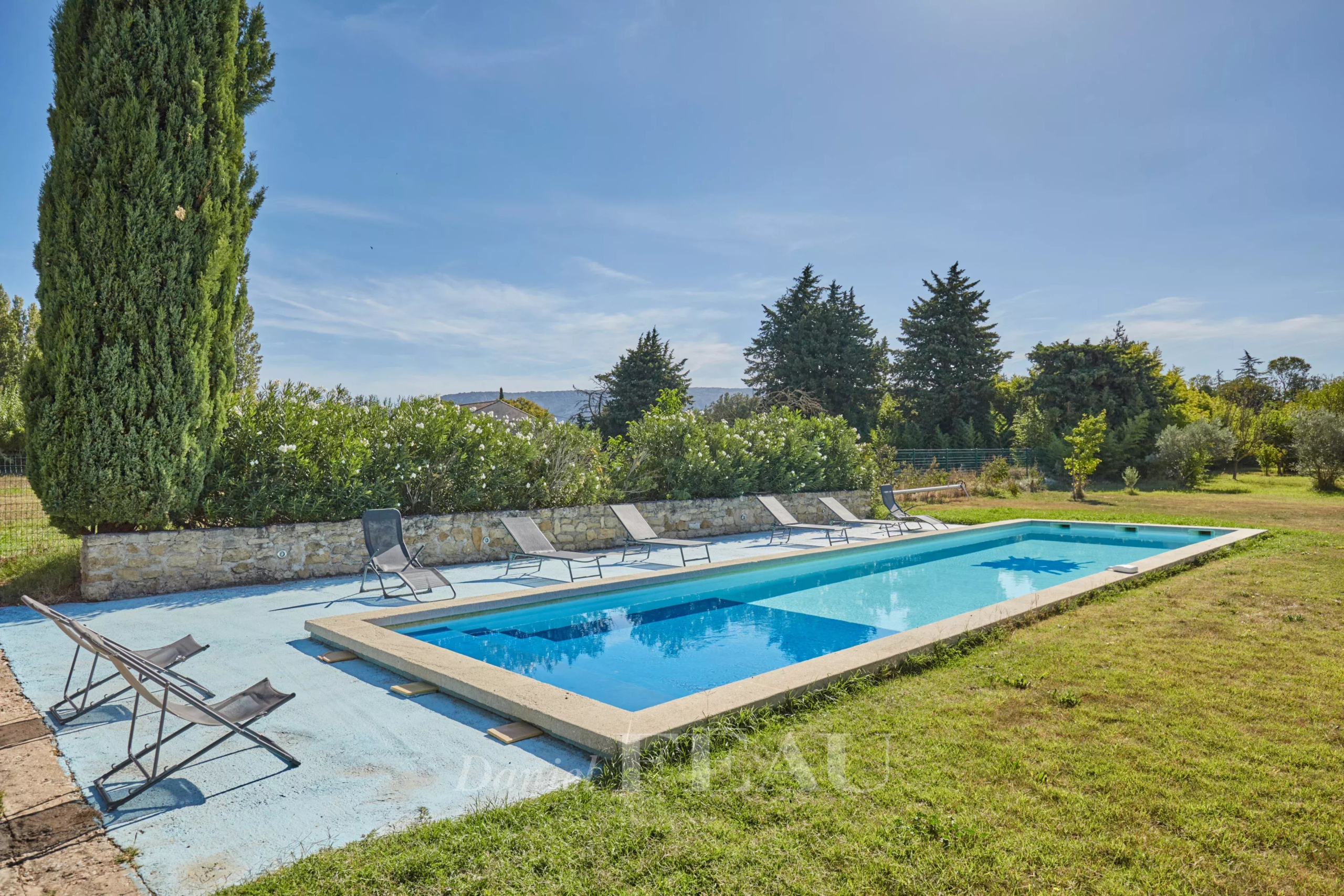 Piscine entourée de chaises longues dans un jardin verdoyant près d'un mas provençal.