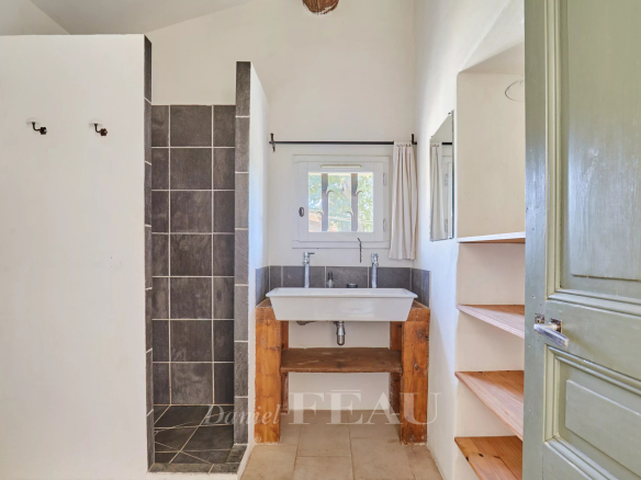 Salle de bain avec douche, lavabo en bois et étagères, murs blancs et carrelage gris.