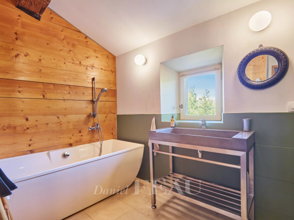 Salle de bain avec baignoire, lavabo en métal et mur en bois, lumière naturelle