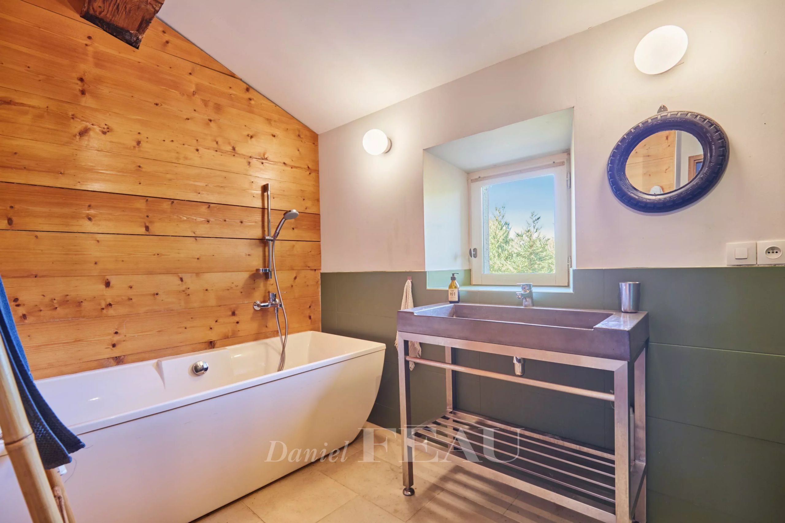 Salle de bain avec baignoire, lavabo en métal et mur en bois, lumière naturelle
