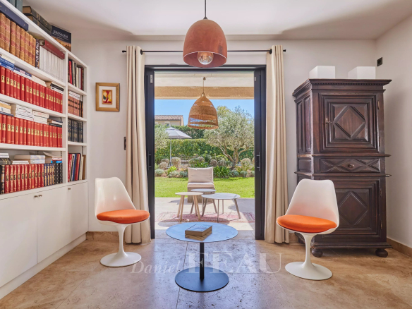 Intérieur d'une maison à Eygalières avec bibliothèque, chaises blanches et vue sur le jardin.
