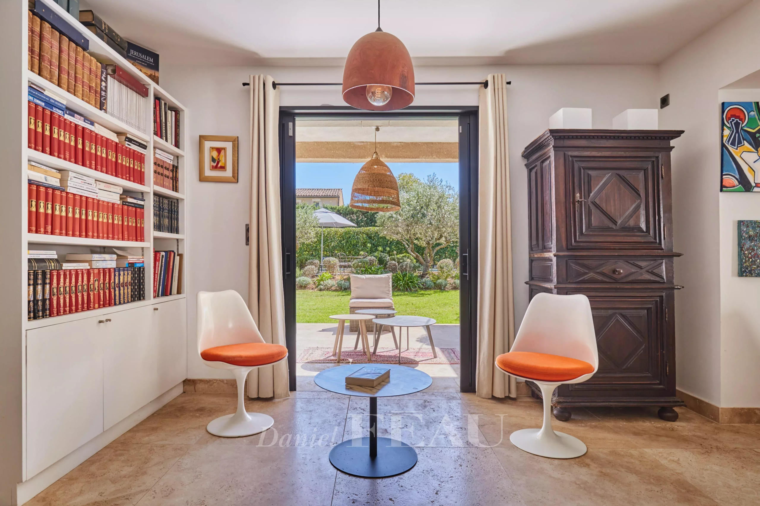 Intérieur d’une maison à Eygalières Intérieur d'une maison à Eygalières avec bibliothèque, chaises blanches et vue sur le jardin.