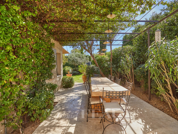 Terrasse d'une maison à Eygalières avec une table en bois et des chaises, entourée de verdure.