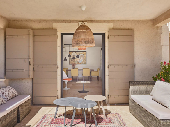 Terrasse d'une maison à Eygalières avec mobilier en osier et vue sur un intérieur lumineux.