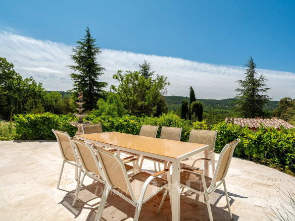 Terrasse d'une villa à Rustrel avec table et chaises, vue sur un paysage verdoyant.