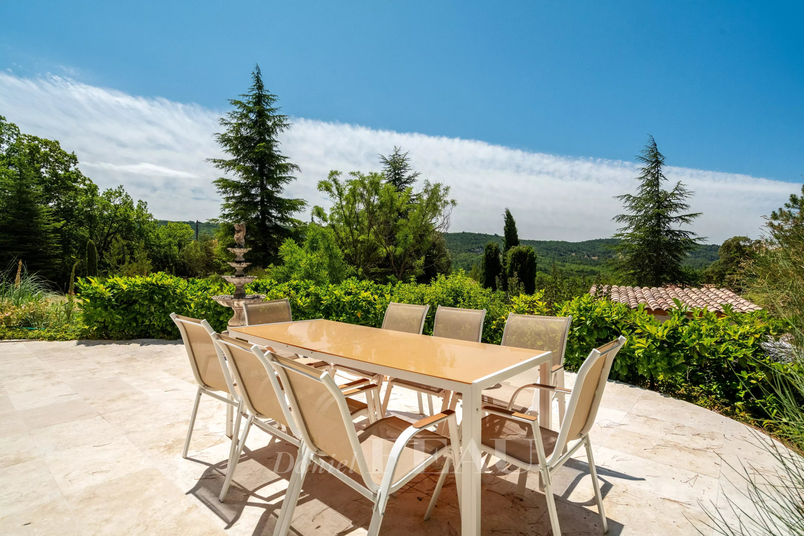 Terrasse d'une villa à Rustrel avec table et chaises, vue sur un paysage verdoyant.