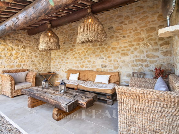 Espace extérieur d'une propriété rénovée avec mobilier en rotin et pierres apparentes à Lourmarin.
