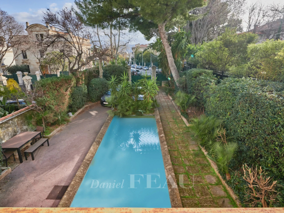Rectangular blue pool flanked by stone edges, with a brick path and lush hedges in a residential garden.