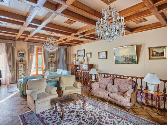 Luxurious living room with a coffered wooden ceiling, crystal chandeliers, and antique seating including a floral pink sofa and beige armchairs.