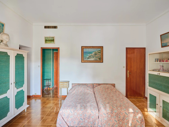 Twin beds with pink floral covers in a vintage bedroom, flanked by white and green-paneled wardrobes and wooden doors.