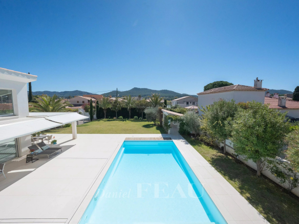 Backyard view of a rectangular blue pool, white tiled patio, lounge chairs under a shade canopy, with a green lawn and houses beyond in distance.