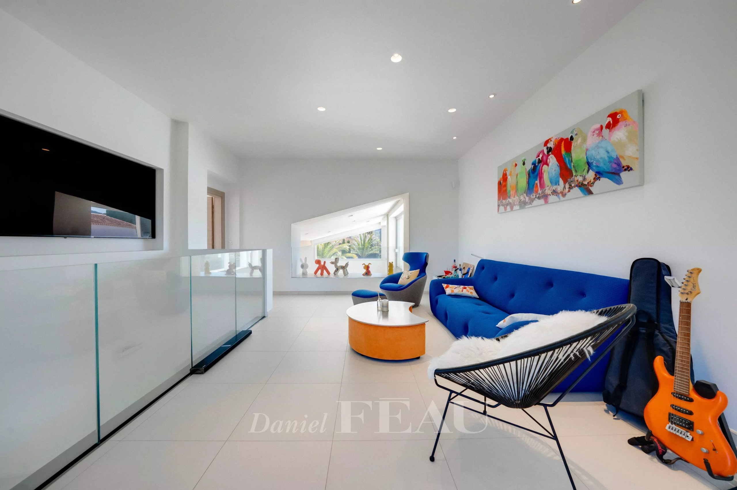 Bright contemporary living room with white walls, a blue sofa, orange round coffee table, and a colorful bird mural on the wall.