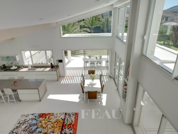 Open-plan kitchen and dining area with white cabinets, an island with stools, and a glass door to a sunny patio beyond the table.