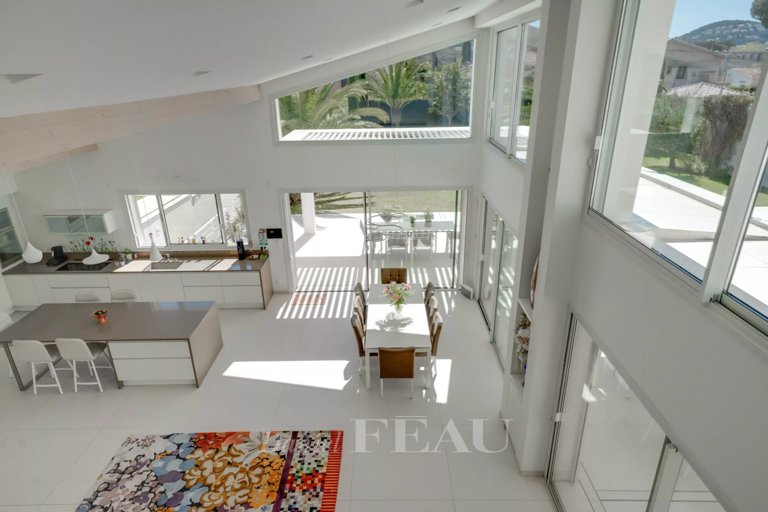 Open-plan kitchen and dining area with white cabinets, an island with stools, and a glass door to a sunny patio beyond the table.