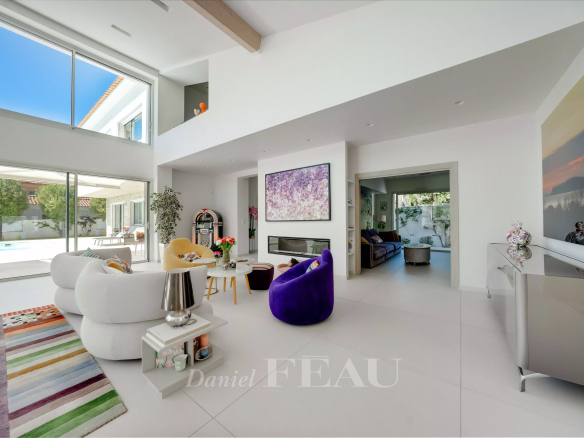 Bright open living room with white furniture, a purple chair, colorful rug, fireplace, and large glass walls showing an outdoor pool.