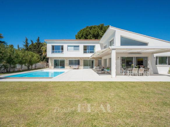 Modern white two‑story home with a rectangular pool, expansive patio, and outdoor dining area under a shaded pergola.