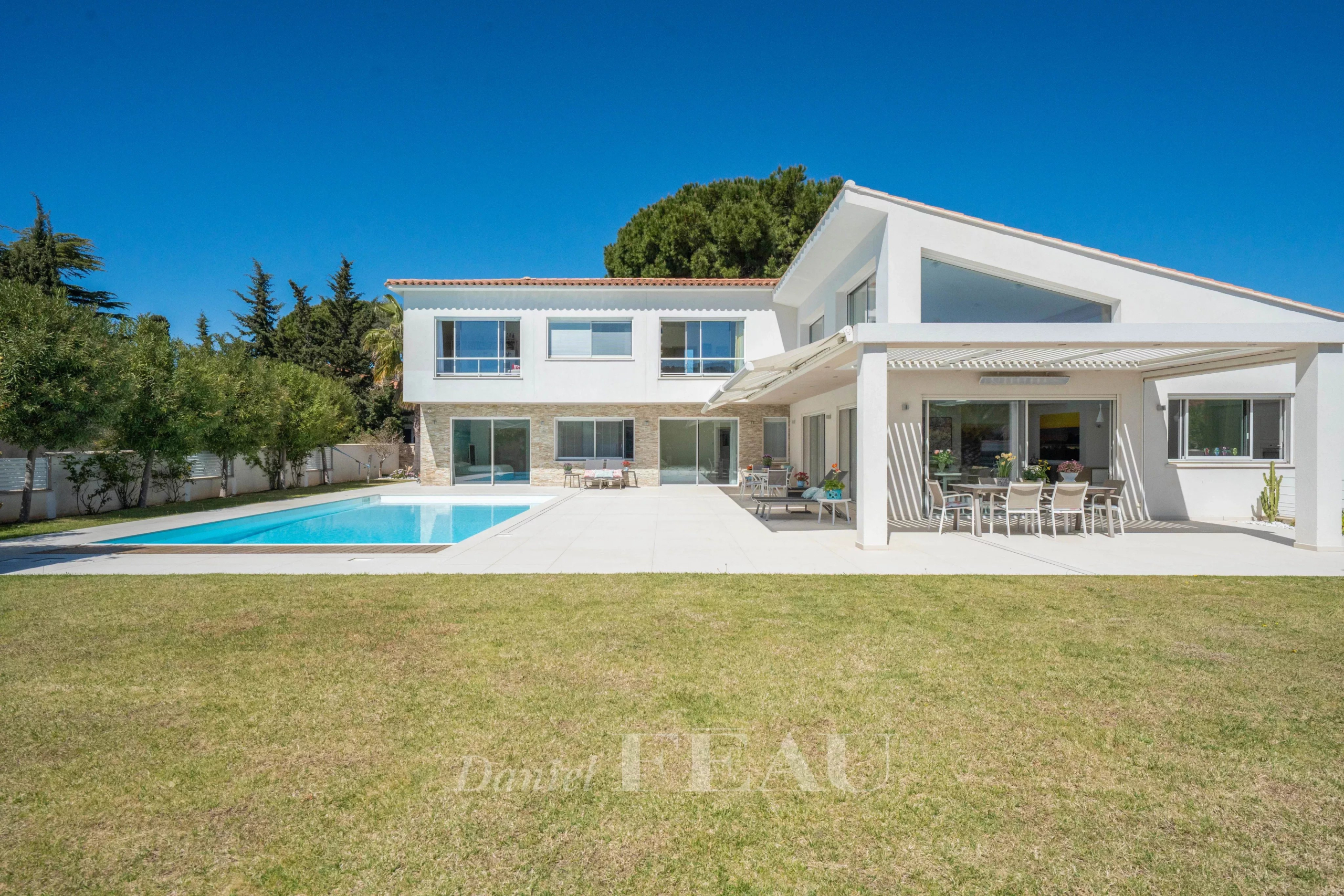 Modern white two‑story home with a rectangular pool, expansive patio, and outdoor dining area under a shaded pergola.
