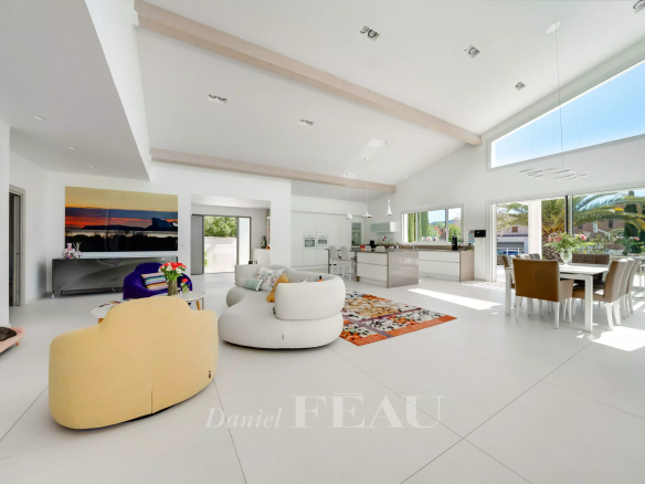 Bright open-concept living area with white walls, curved beige sofa, colorful rug, and a modern kitchen.