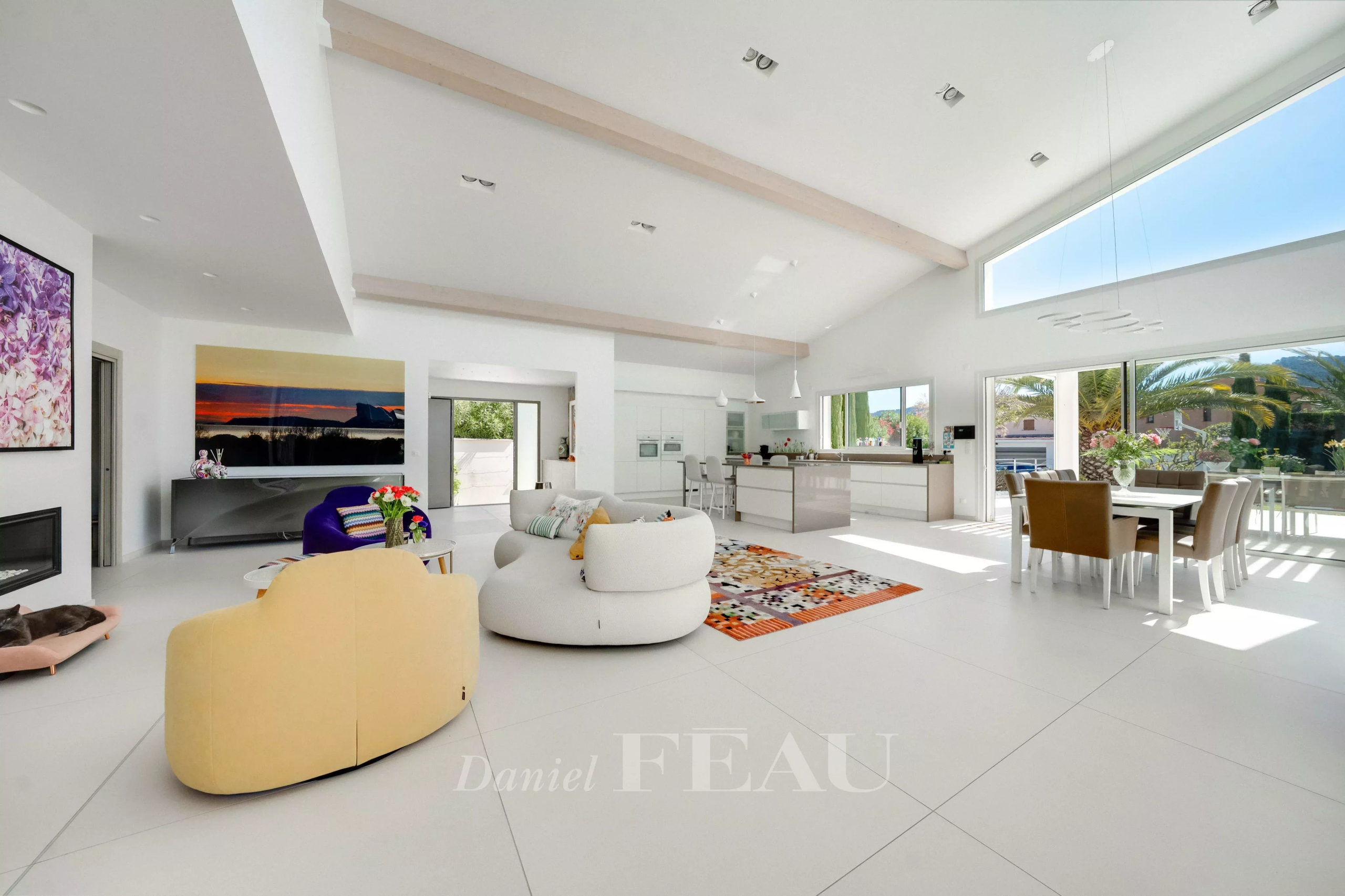 Bright open-concept living area with white walls, curved beige sofa, colorful rug, and a modern kitchen.