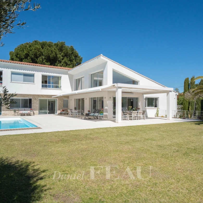 White modern house with a rectangular pool, covered patio, and outdoor seating on a sunny day.