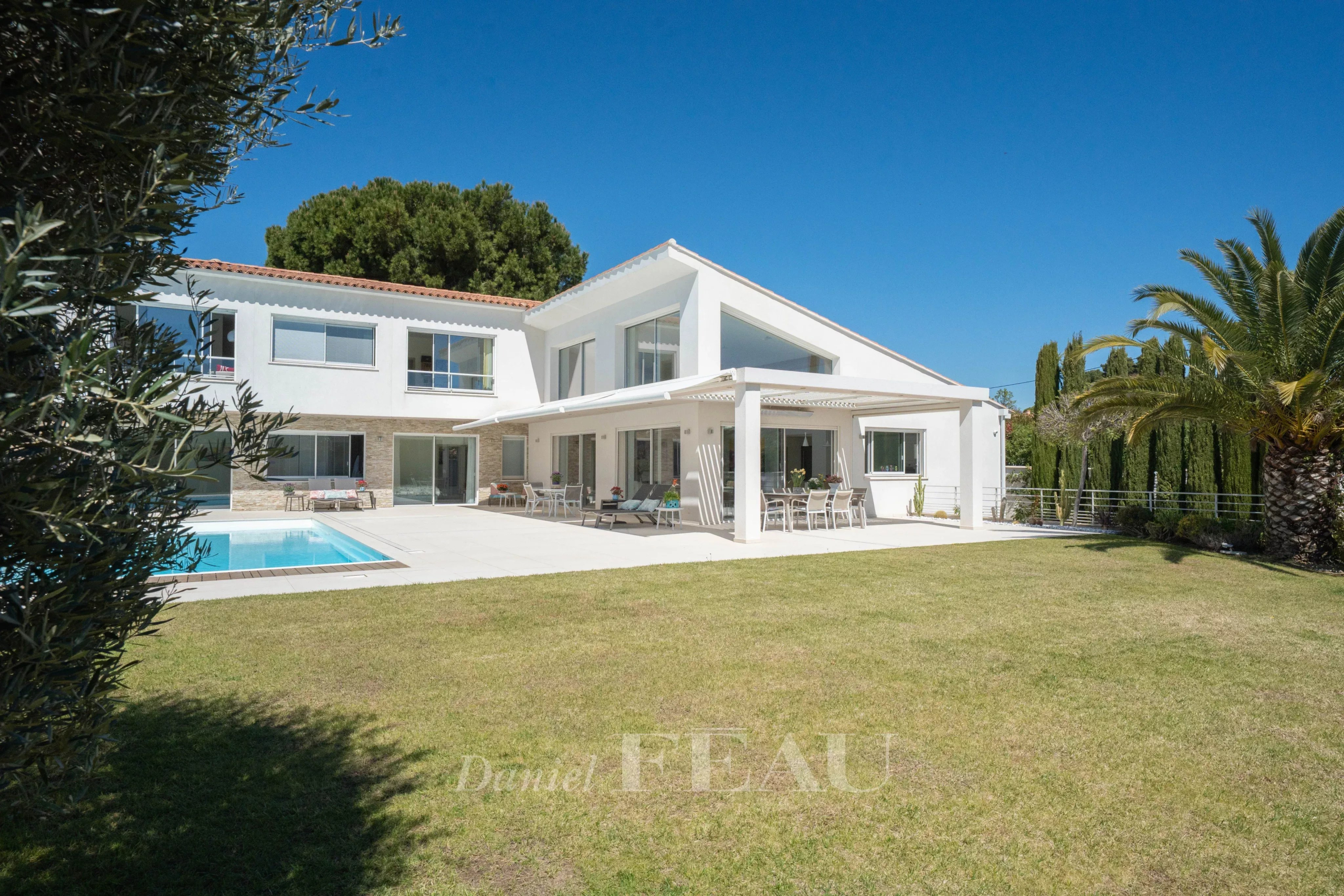White modern house with a rectangular pool, covered patio, and outdoor seating on a sunny day.