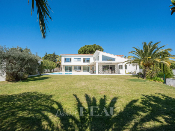 White contemporary two-story house with a rectangular pool in a spacious lawn and palm trees under a clear blue sky.