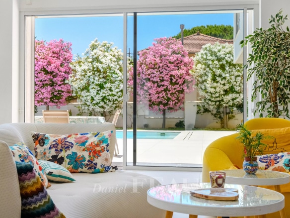 Intérieur d'une villa contemporaine avec un séjour lumineux et vue sur des fleurs colorées.