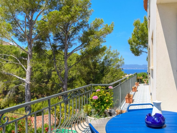 Balcon d'une maison rénovée à Saint-Cyr-sur-Mer avec vue sur la mer et des arbres environnants.
