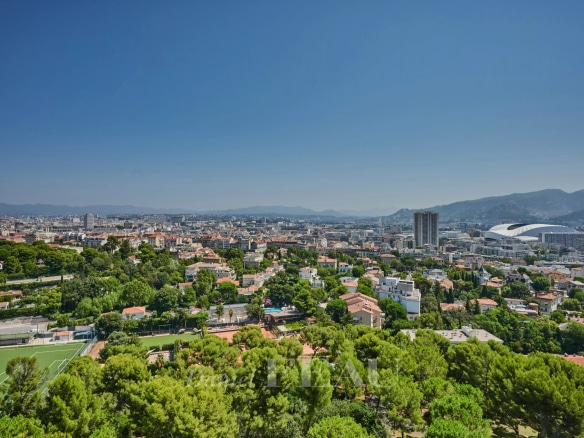 Vue panoramique sur Marseille depuis un dernier étage, avec des bâtiments et des espaces verts visibles.