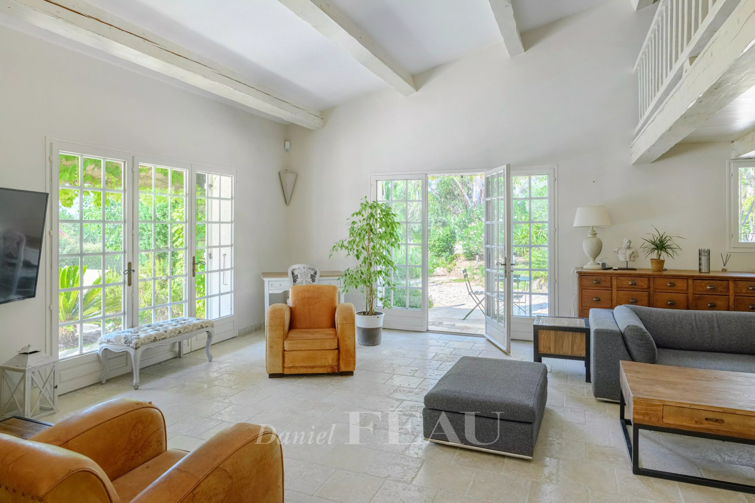 Interior of a house with a bright living room, windows open onto the garden.