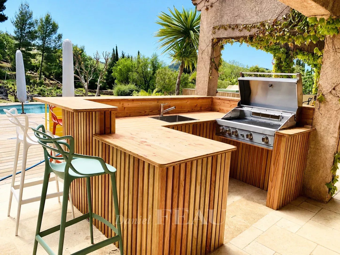 Cuisine extérieure en bois avec barbecue près de la piscine dans un domaine provençal.