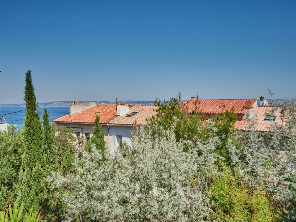 Vue sur des toits et la mer depuis un jardin verdoyant à Marseille 7ème.
