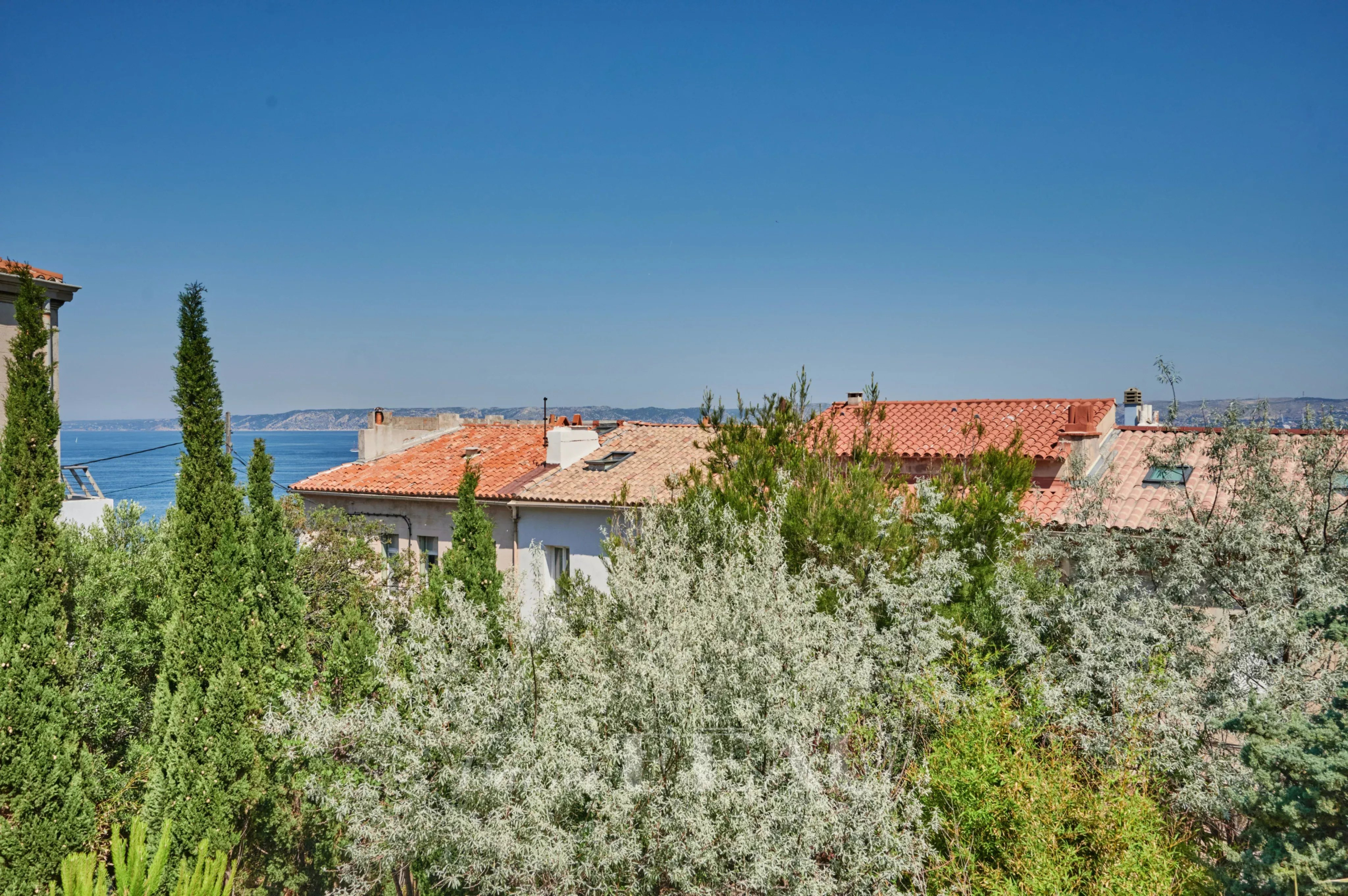 Vue sur des toits et la mer depuis un jardin verdoyant à Marseille 7ème.