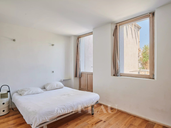 Chambre lumineuse avec lit simple et fenêtres sur deux côtés.