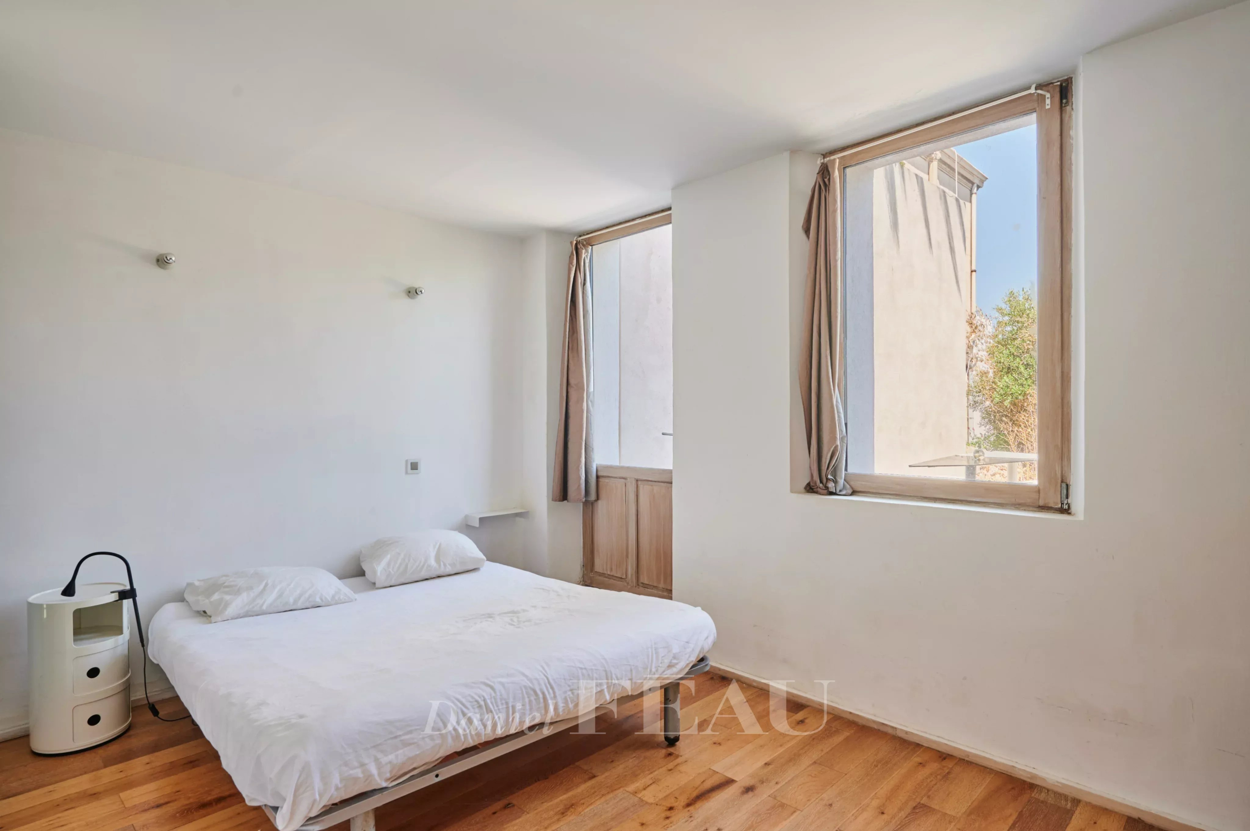 Chambre lumineuse avec lit simple et fenêtres sur deux côtés.
