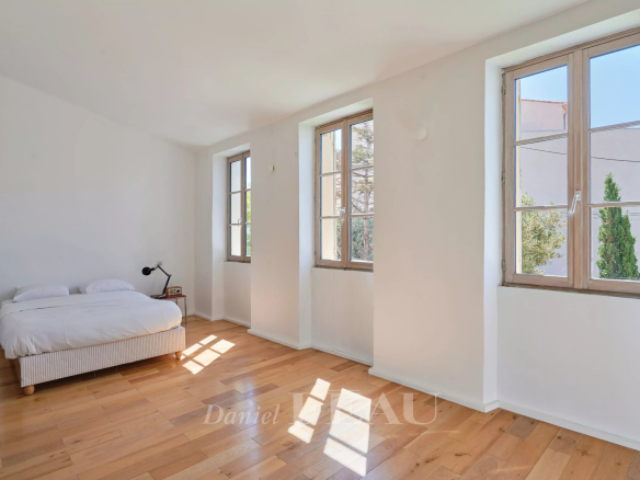 Chambre lumineuse avec fenêtres sur trois côtés, parquet en bois et lit simple.
