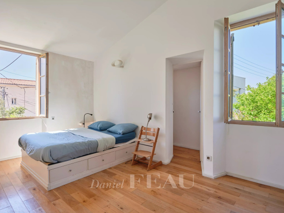 Chambre lumineuse avec lit simple et fenêtres ouvertes, parquet en bois.