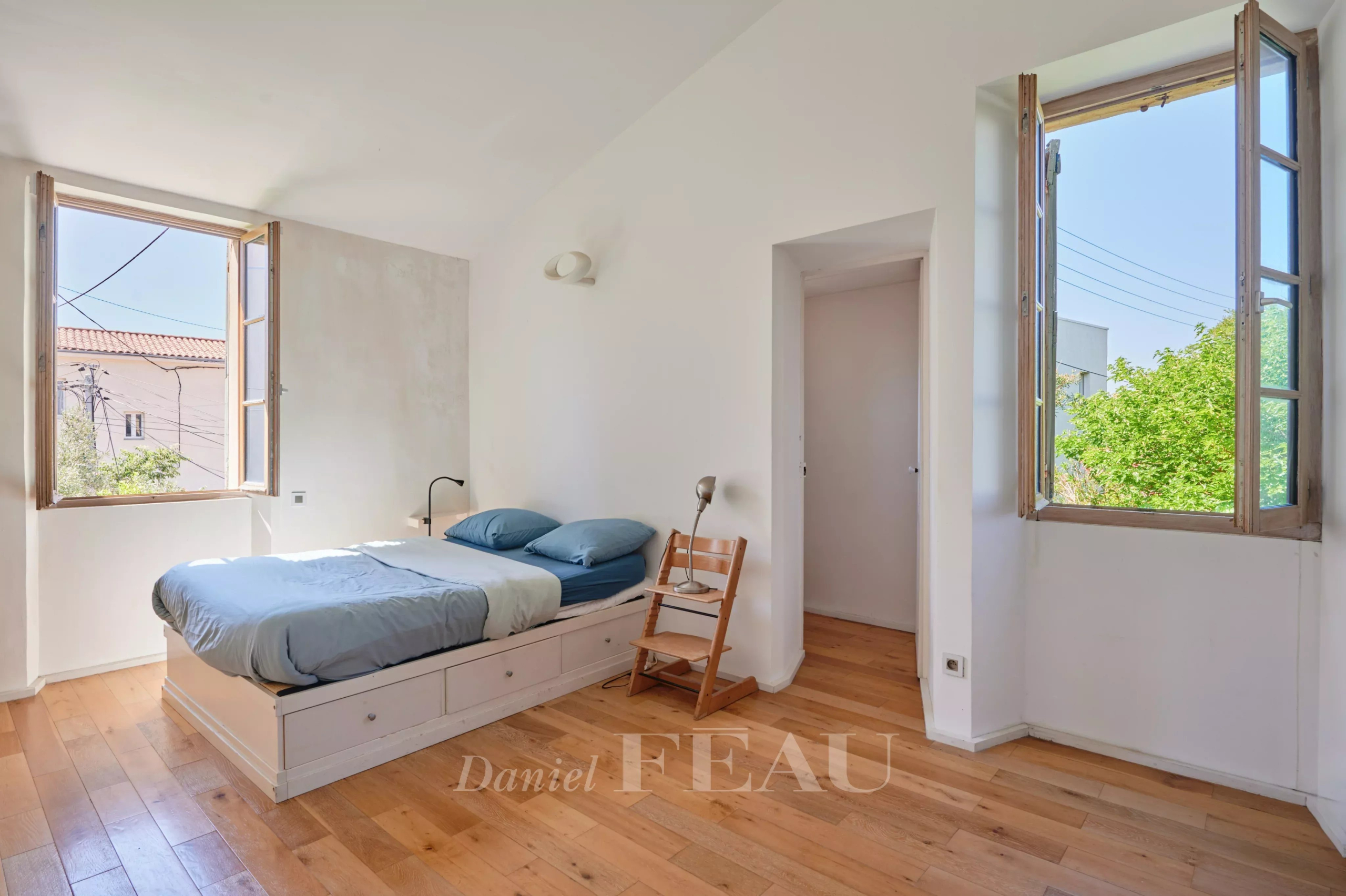 Chambre lumineuse avec lit simple et fenêtres ouvertes, parquet en bois.