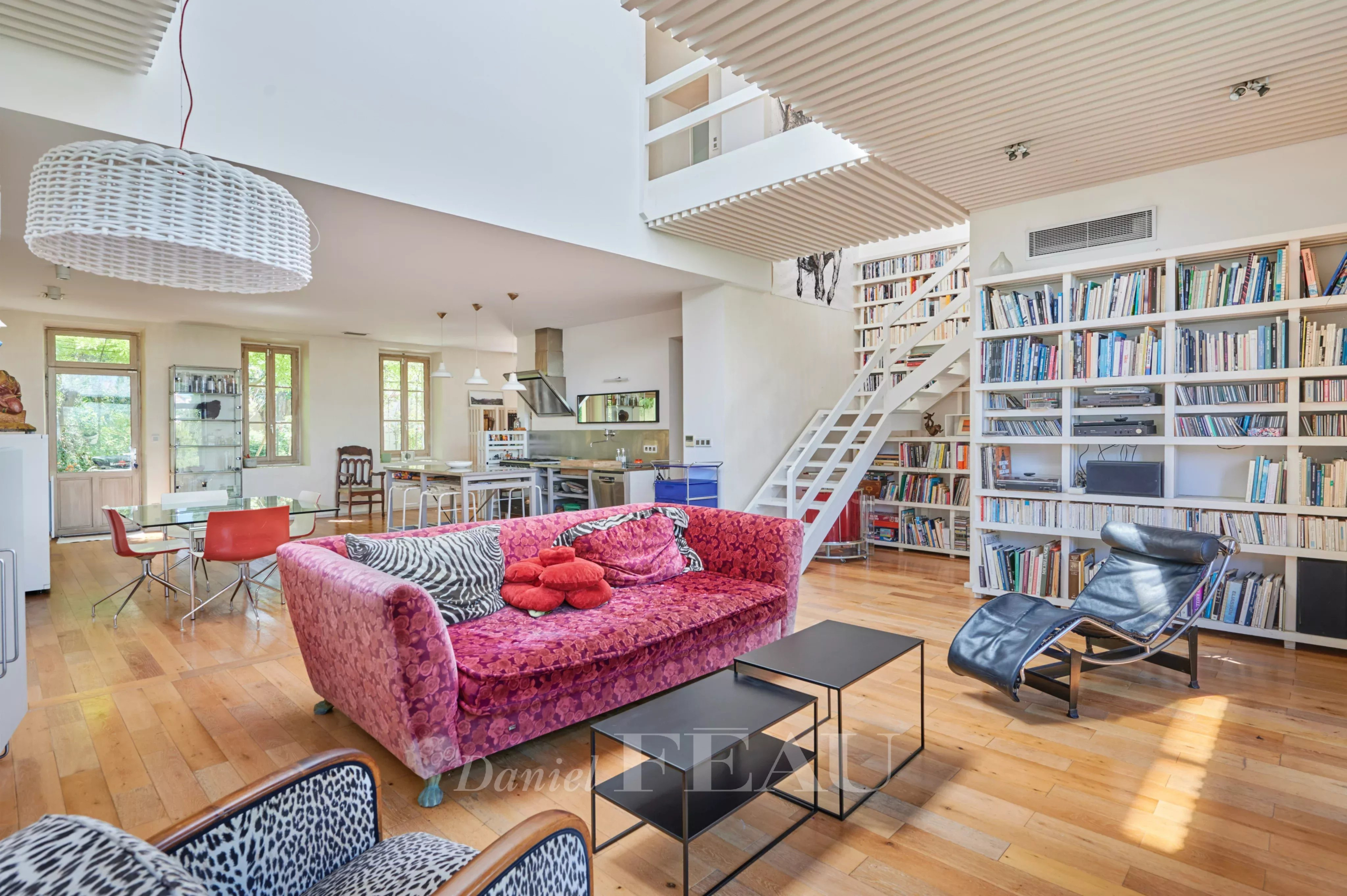 Intérieur d'une maison moderne avec salon lumineux, bibliothèque et cuisine ouverte.