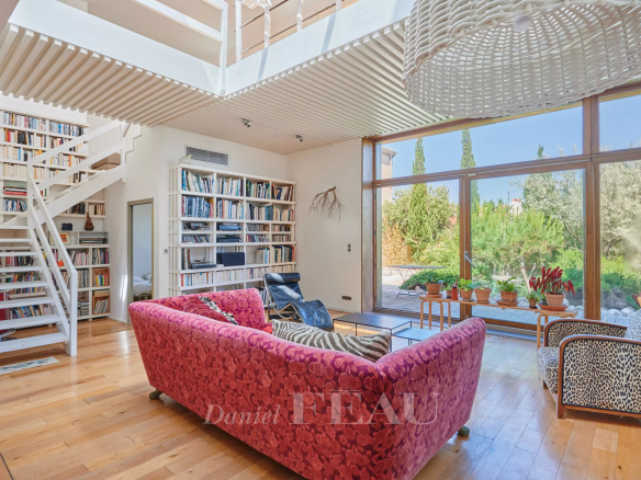 Intérieur d'une maison moderne avec un salon lumineux, des étagères et un jardin visible à travers les grandes fenêtres.