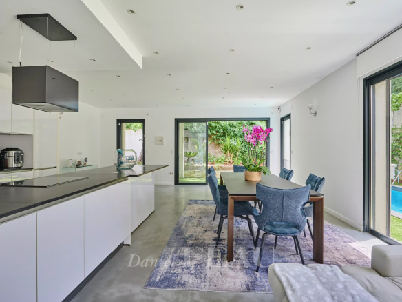 Intérieur d'une maison contemporaine avec cuisine ouverte et salle à manger, vue sur le jardin et la piscine.